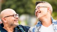 Two men arm laughing as they walk together on the street.